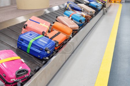 Bright colorful suitcases and bags on luggage conveyor belt at arrival area of passenger terminal in airport. Baggage carousel.