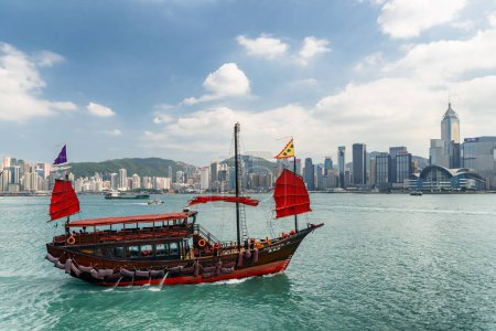 Foto de Hong Kong - 20 de octubre de 2017: Fabulosa vista del tradicional velero chino de madera con velas rojas en el puerto de Victoria. El horizonte de la isla de Hong Kong en un día soleado. Increíble paisaje urbano. - Imagen libre de derechos