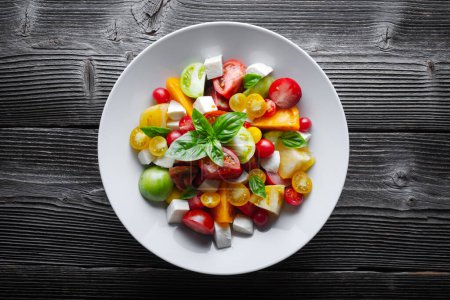 Téléchargez les photos : Salad with different varieties kind of red, yellow, green and black tomato mix, mozzarella cheese and basil. Caprese salas with fresh colourful tomatoes. Food photography - en image libre de droit