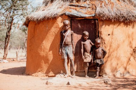 Foto de OPUWO, OTJIWARONGO REGION NAMIBIA - 4 DE MAYO DE 2021: Jóvenes niños Himba no identificados con el collar típico en el museo viviente de Himba durante una aparición frente a los turistas - Imagen libre de derechos