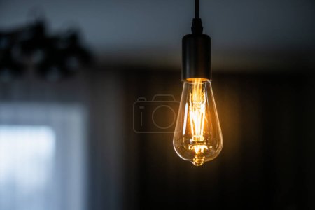 Foto de Vintage hanging Edison light bulb with warm light over dark home background - Imagen libre de derechos