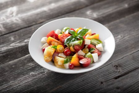 Photo for Salad with different varieties kind of red, yellow, green and black tomato mix, mozzarella cheese and basil. Caprese salas with fresh colourful tomatoes. Food photography - Royalty Free Image