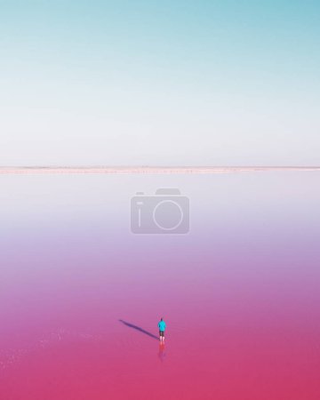 Téléchargez les photos : Homme solitaire en bleu accaparé dans l'eau rose du lac sous un ciel bleu clair dans la journée d'été. Concept de couleur créative - en image libre de droit