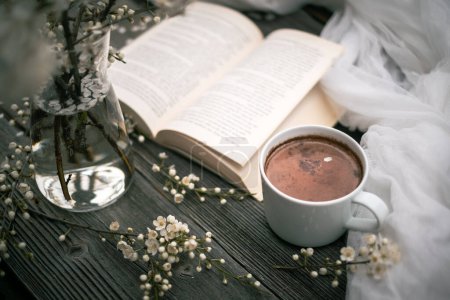 Téléchargez les photos : Coupe de cacao au chocolat chaud, vieux livre et fleurs de cerise de printemps sur fond en bois. Concept de lecture - en image libre de droit