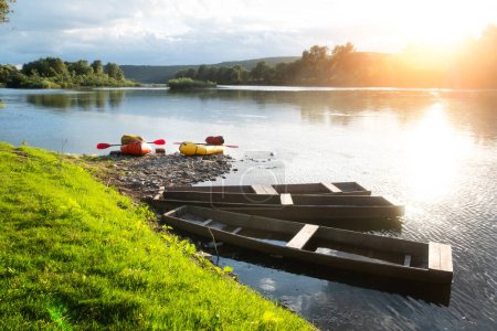 Téléchargez les photos : Embarcations en caoutchouc orange et jaune sur une rivière au lever du soleil près de vieux bateaux en bois. Emballage et concept de vie active - en image libre de droit