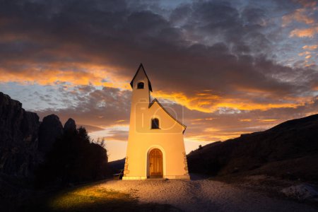 Foto de Vista de Gorgeus en la pequeña capilla iIlluminated - Kapelle Ciapela en Gardena Pass, montañas Dolomitas italianas. Luz dorada al atardecer sobre fondo. Dolomita Alpes, Italia. Paisaje fotografía - Imagen libre de derechos