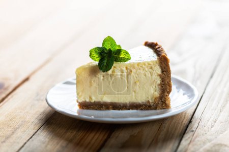 Piece of classic New York cheesecake with a sprig of mint on a plate on a wooden table. The concept of bakery and sweet cakes desserts