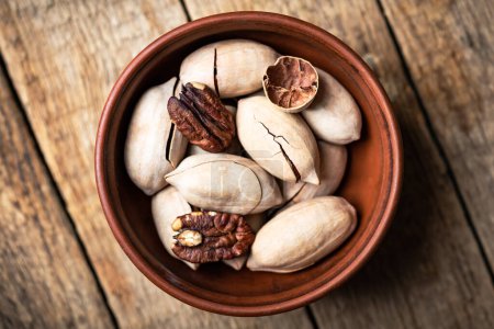 Photo for Dried organic Pecan nuts in orange ceramic bowl on wooden table closeup. Food photography - Royalty Free Image