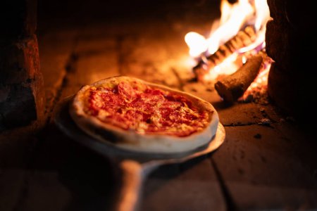 Foto de El pepperoni de pizza italiano se cocina en un horno a leña. Pizza con salami en la pala de pizza en el horno caliente de cerca. Fotografía alimentaria - Imagen libre de derechos