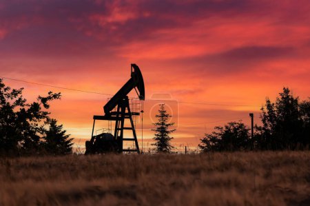 Photo for Oil pump against incredible orange sunset sky. Industrial concept. Pump jack silhouette on evening field. - Royalty Free Image