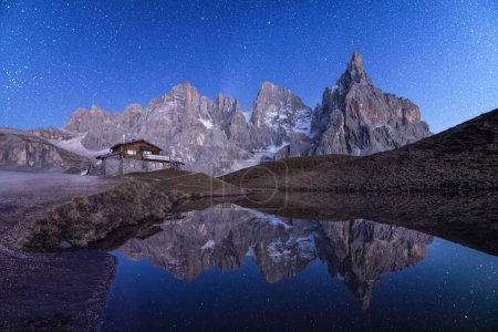 Foto de Increíble paisaje nocturno con un reflejo del cielo estrellado y las montañas en un agua de un pequeño lago en un destino turístico popular Baita Segantini refugio de montaña. Rolle Pass, Dolomitas Alpes, Italia - Imagen libre de derechos