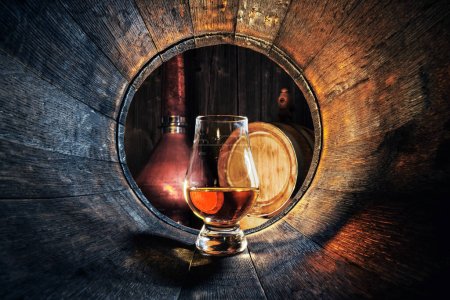 Un vaso de whisky en barrica de roble viejo. Copper alambic en el fondo. Concepto tradicional de destilería de alcohol
