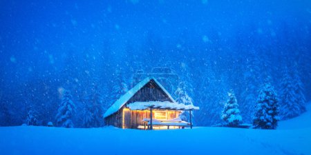 Photo for Solitary mountain cabin tucked away in a snowy forested meadow with evergreen trees in a winter setting. Christmas postcard. Snowy mountains forest - Royalty Free Image