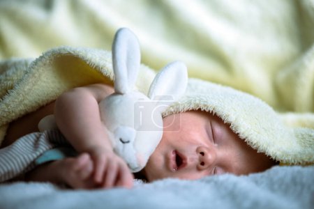 Photo for Little newborn boy sleeps with his favorite toy bunny in a cozy warm bed - Royalty Free Image