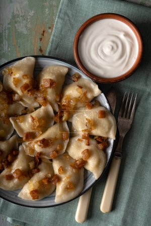 Photo for Traditional Ukrainian food - dumplings varenik with sour cream close up. Fried bacon and onion covers them on top. Food photography - Royalty Free Image