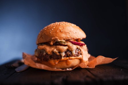 Téléchargez les photos : Petit cheeseburger appétissant sur papier sulfurisé sur table en bois. Photographie alimentaire - en image libre de droit