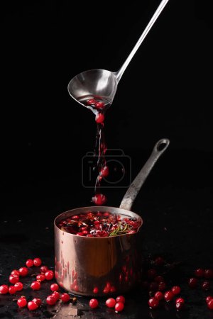 Photo for Mulled wine with cranberries pouring into copper pot from metal ladle on black background. Food photography - Royalty Free Image