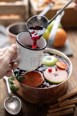 Photo for Mulled wine with slices of orange, apple, cinnamon, star anise, rosemary and cranberries pouring into mug. Food photography - Royalty Free Image