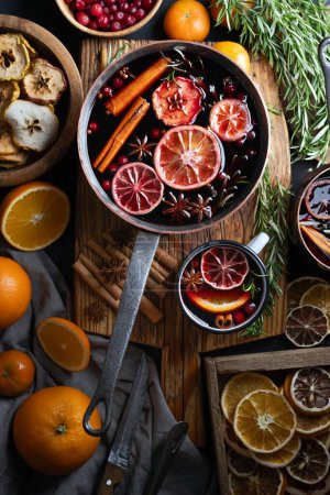 Photo for Copper pot of mulled wine with slices of orange, apple, cinnamon, star anise, rosemary and cranberries on wooden table. Food photography - Royalty Free Image