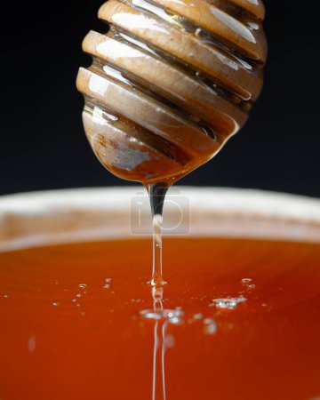 Natural organic honey dripping, pouring from wooden honey dipper close up