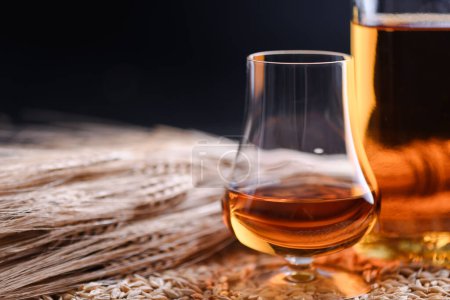 Foto de Un vaso de whisky con orejas de botella y cebada sobre granos de cebada como fondo. Concepto de destilería de whisky - Imagen libre de derechos