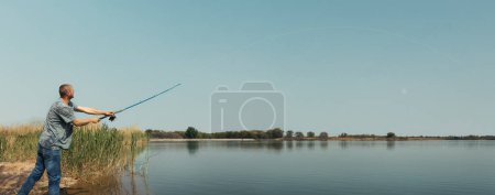 Fischer mit Angelrute allein am Ufer des Flusses. Ruhe und Entspannung in der Natur genießen. Weitwinkelaufnahme