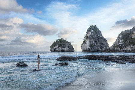 A girl in a swimsuit is standing on the stone. View of Diamond Beach, Nusa Penida, Bali, Indonesia. A small island in the ocean. Wallpaper background. Natural landscapes.