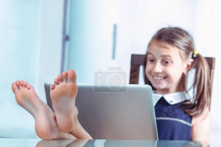 Photo for Humorous image of cheerful caucasian young girl took off her shoes, put her feet on the desktop and working in office with bare feet. Selective focus on feet. Horizontal image. - Royalty Free Image