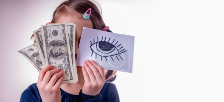 Conceptual photography: double standards. A young girl is holding US Dollar bills and banner with an open eye as a symbol of trickery, double standards and selective justice. Copy space.