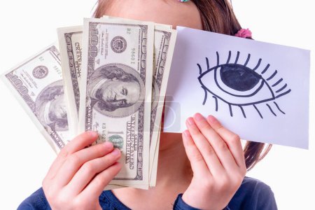 Conceptual photography: double standards. A young girl is holding US Dollar bills and banner with an open eye as a symbol of trickery, double standards and selective justice. Horizontal image.