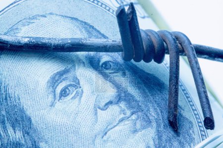 Wirtschaftliche Konfrontation und Krieg, Sanktionen und Embargo-Zerschlagung. Stacheldraht gegen US-Dollar-Schein. Selektiver Fokus auf die Augen Benjamin Franklins. Horizontales Bild.