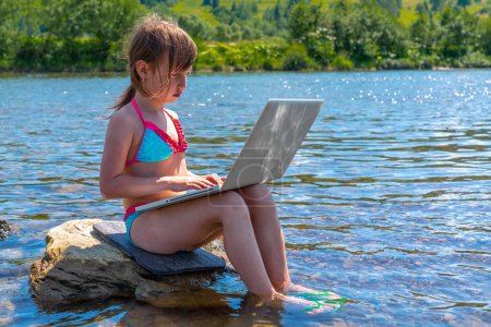 Portrait of young girl using and learning with laptop computer while traveling mountains and river. Copy space for text or design.