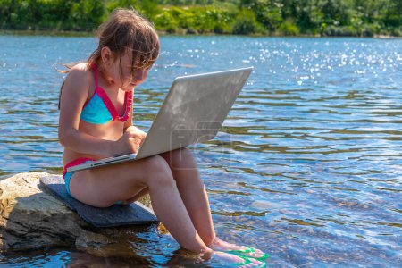 Young girl using and learning with laptop computer while traveling mountains and river. Copy space for text or design.