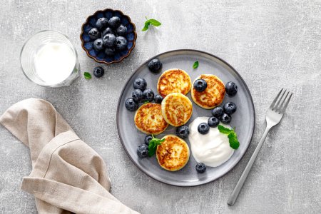 Photo for Cottage cheese fritters with fresh blueberry and yogurt for breakfast, copy space, view from above - Royalty Free Image