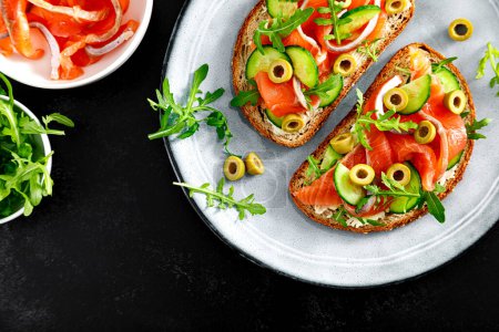 Photo for Toasts with salted salmon, arugula, green olives and cucumber, copy space, top down view - Royalty Free Image