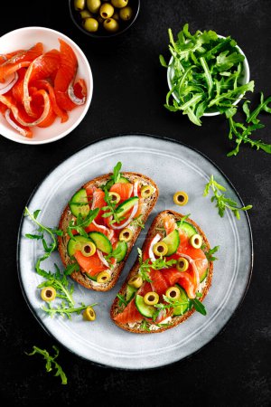 Photo for Toasts with salted salmon, arugula, green olives and cucumber, top down view - Royalty Free Image