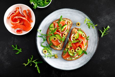 Photo for Toasts with salted salmon, arugula, green olives and cucumber, top down view - Royalty Free Image