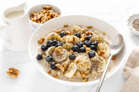 Photo for Oatmeal bowl. Oat porridge with banana, blueberry, walnut, chia seeds and oat milk for healthy breakfast. Healthy diet food - Royalty Free Image