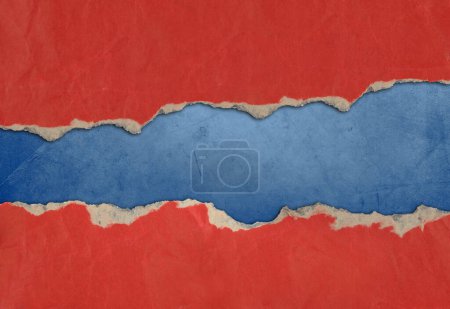 Photo for Hole ripped in red paper on blue background. Copy space - Royalty Free Image