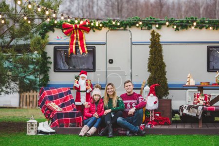 Photo for Happy caucasian family is sitting on the wooden floor in front of the trailer house with Christmas decorations - Royalty Free Image