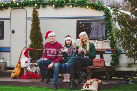 Photo for Happy caucasian family is drinking tea or cocoa in front of the trailer house with Christmas decorations - Royalty Free Image
