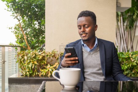 Téléchargez les photos : Portrait d'un bel homme d'affaires africain noir utilisant le téléphone et prenant une pause café - en image libre de droit