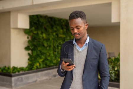 Téléchargez les photos : Portrait de bel homme d'affaires africain noir portant costume et textos avec téléphone intelligent - en image libre de droit
