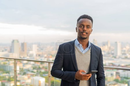 Téléchargez les photos : Portrait d'un bel homme d'affaires africain noir portant un costume et tenant un téléphone intelligent - en image libre de droit