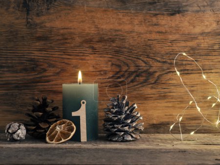 Photo for Candle of the first Advent burns, pine cones and Christmas decoration on wood with Christmas lights - Royalty Free Image