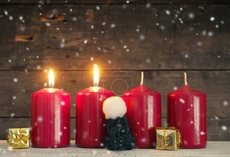 Four red Advent candles on a rustic wooden background, second candle is burning, Christmas concept background