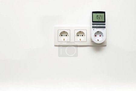 Photo for White triple outlet with inserted timer socket, installed on the white wall, front view. - Royalty Free Image