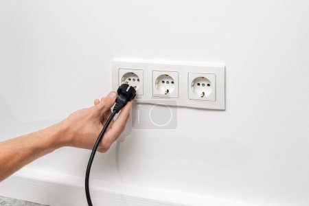 Photo for Human hand unplugging black cable from triple white electrical outlet on the white wall - Royalty Free Image