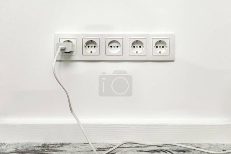 Photo for White five-way wall power socket installed on white wall with phone adapter inserted - Royalty Free Image