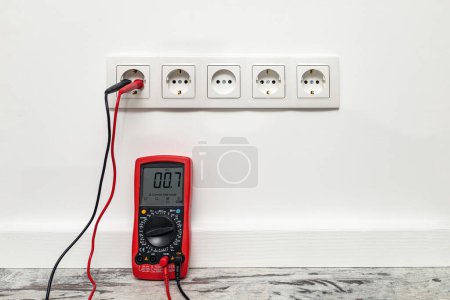 Photo for White five-way wall power socket installed on the white wall. Multimeter measures voltage, lack of electricity - Royalty Free Image
